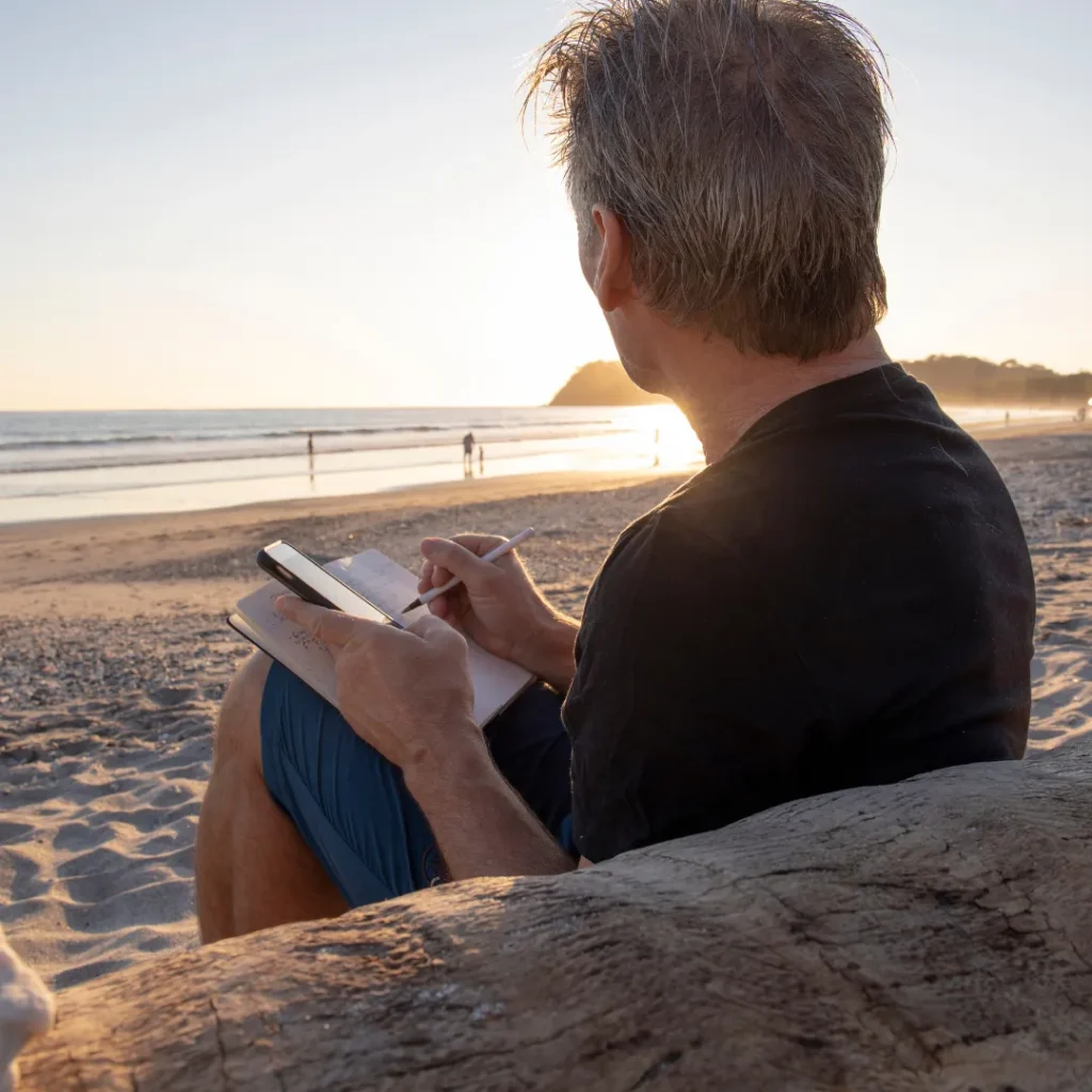 man at beach journaling and watching the ocean